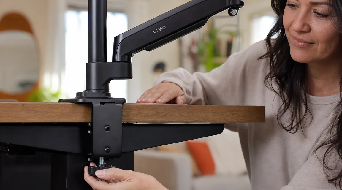 Close-up of the VIVO monitor arm clamp attached to a desk edge, showing the clamp jaw and tightening knob